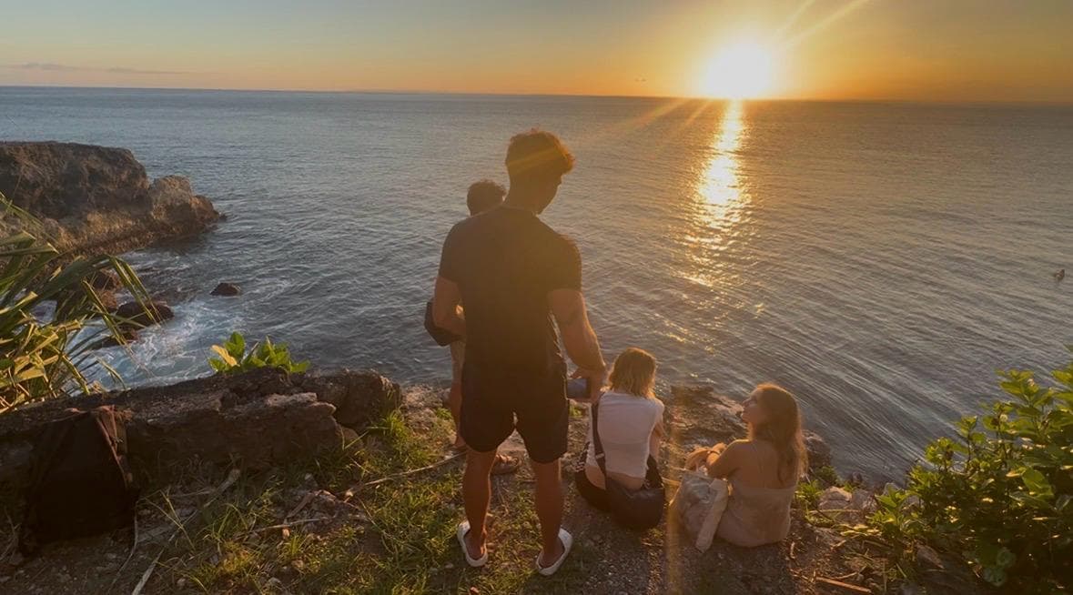 A group of people watching the sunset over the ocean from a rocky coastal cliff