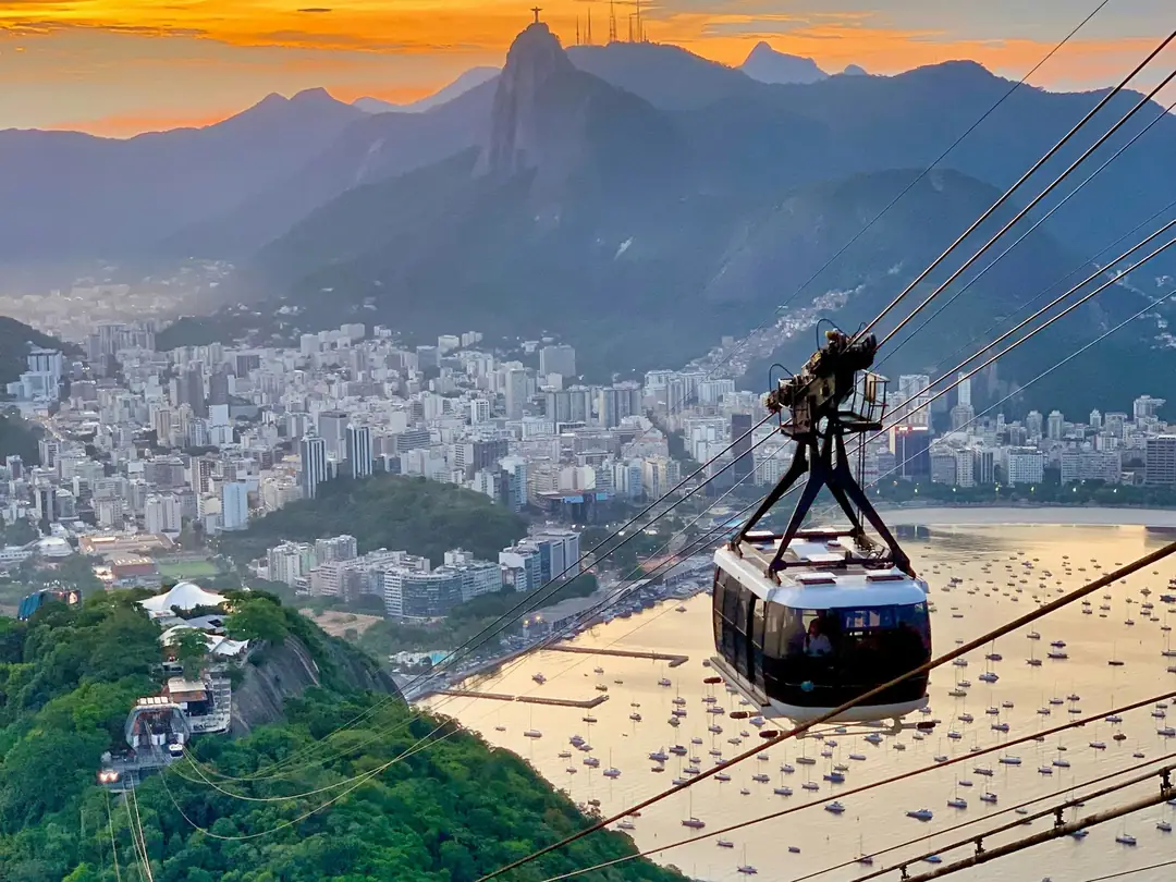 A cable car above Rio de Janeiro at sunset, with Botafogo Bay and the mountains behind